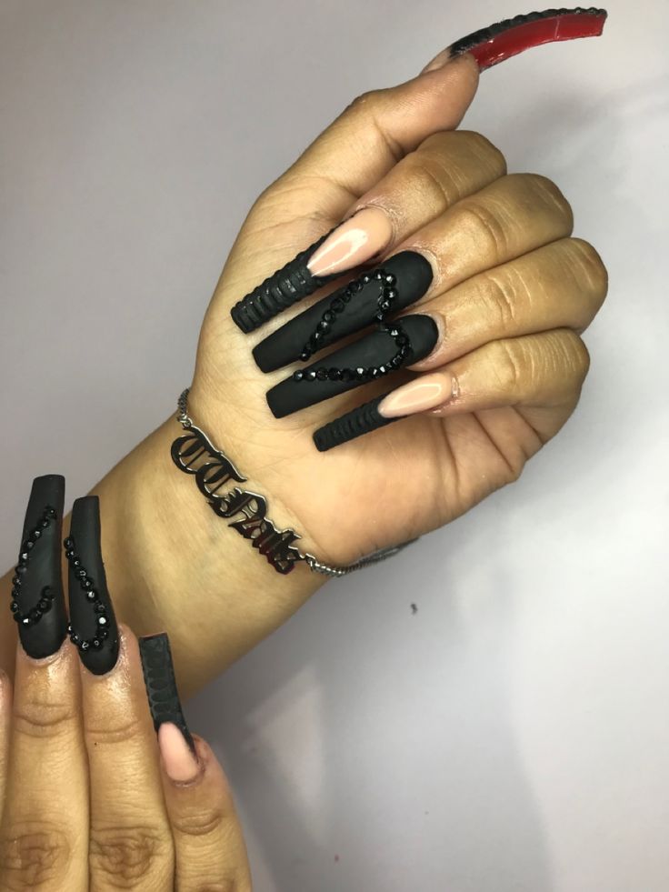 Edgy Elegance: Striking Black Matte Nails with Glamorous Embellishments and a Nude Accent.