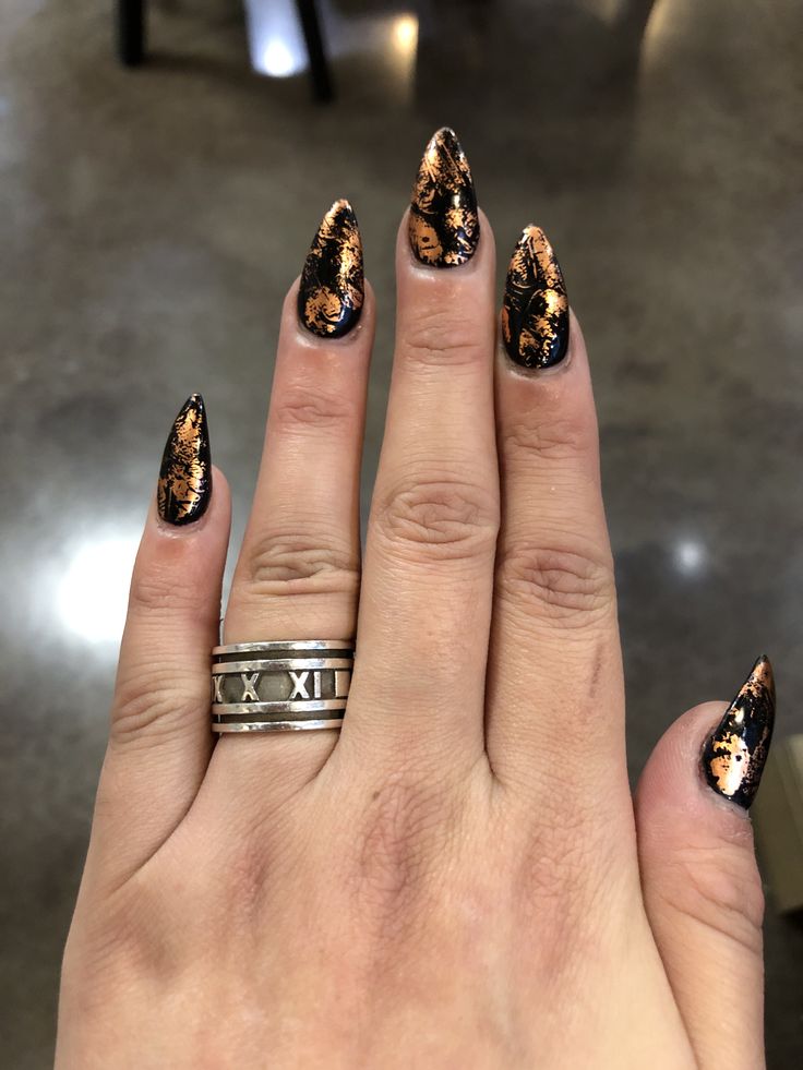 Elegant Long Pointed Nail Design with Copper Detailing on Black Base.