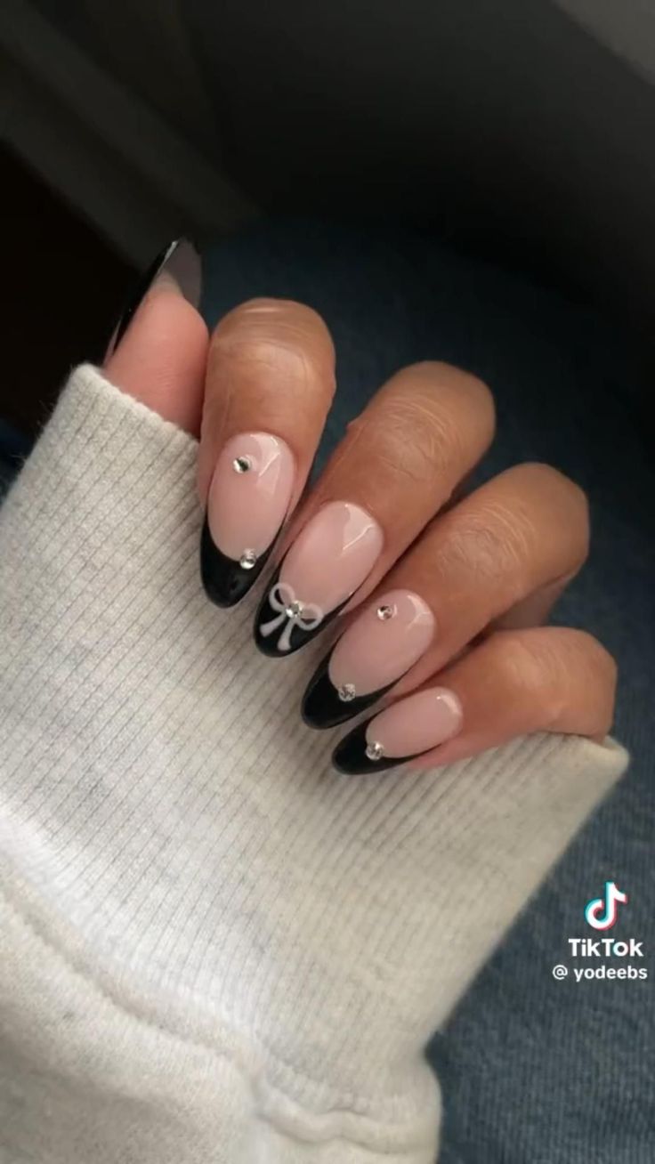 Stylish Nail Design: Playful Soft Pink and Glossy Black Tips with Bow and Rhinestone Accents.