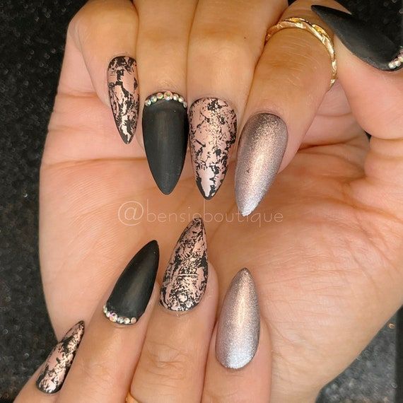 Sophisticated Nail Design: Matte Black and Metallic Finishes with Textured Patterns and Rhinestone Embellishments.