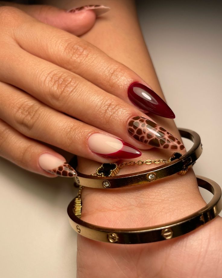 Sophisticated Almond-Shaped Nail Design in Burgundy and Nude with Bold Animal Print Accents and Gold Bangles.