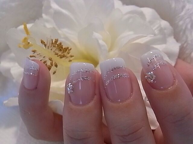 Elegant French Tip Nail Design with Shimmering Silver Accents and Glamorous Embellishments.