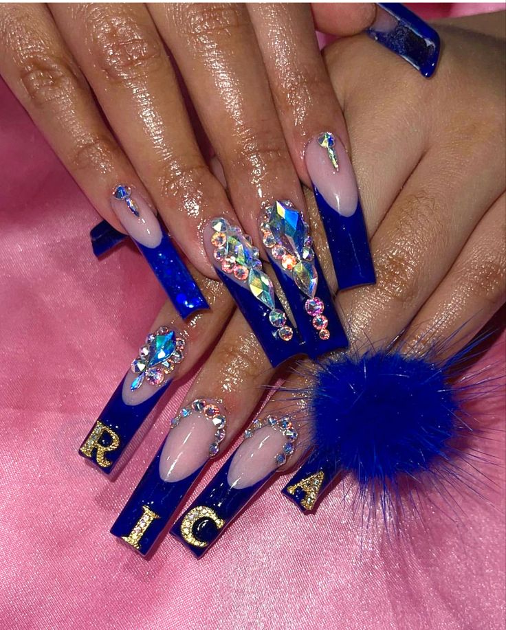 Glamorous Bold Blue Acrylic Nails with Rhinestones, Geometric Designs, and Pom-Pom Accents.