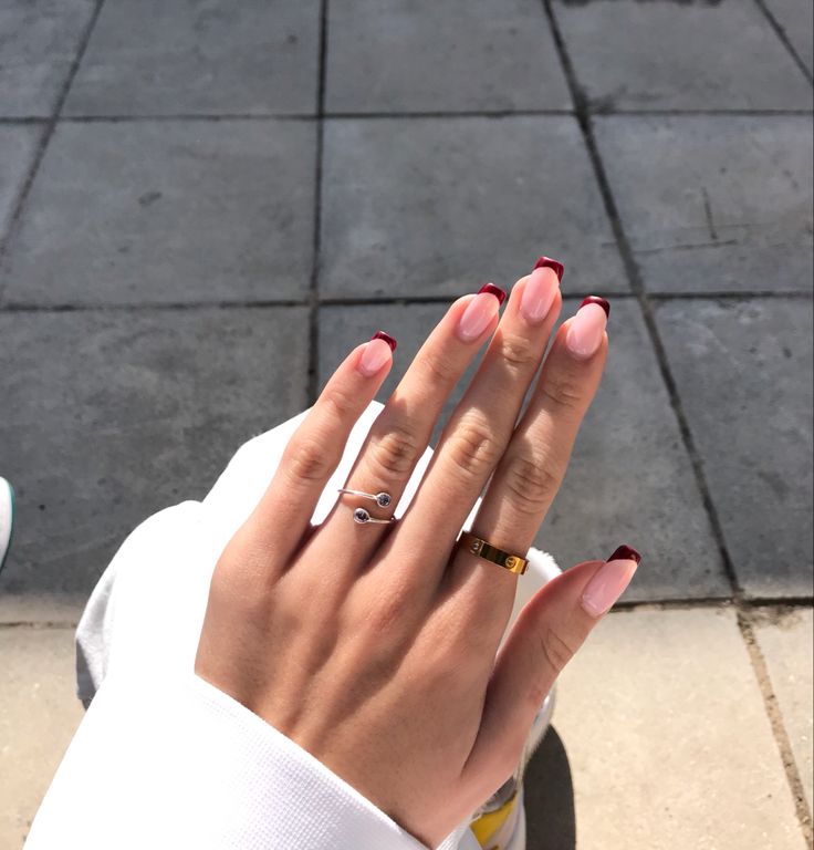 Chic Soft Pink Nail Design with Striking Crimson Tips and Delicate Ring Accents.