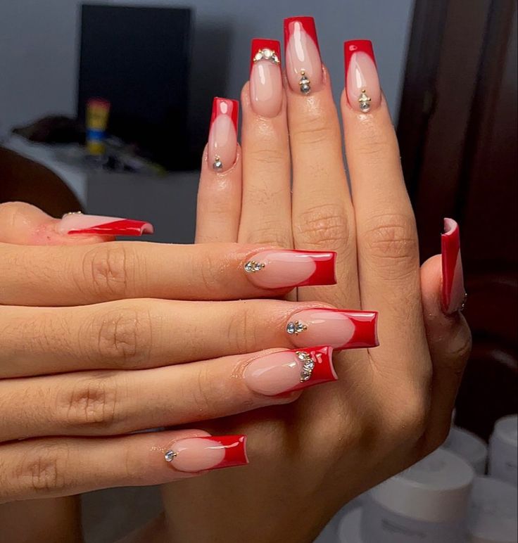 Elegant Red French Tip Nail Design with Nude Base and Rhinestone Accents.