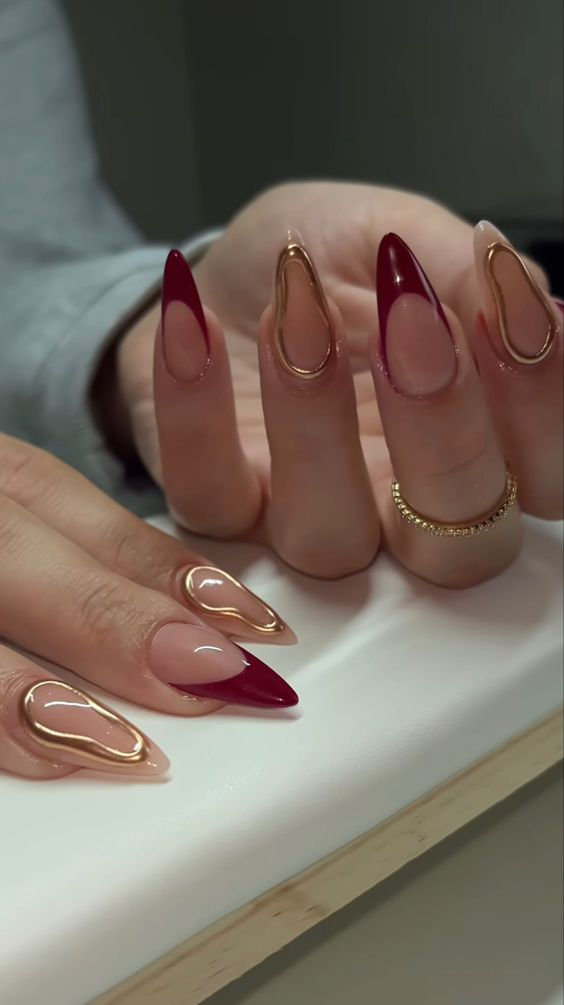 Sophisticated Nail Design: Sharp Almond Shapes and Soft Curves with Deep Red Tips and Glossy Gold Accents.