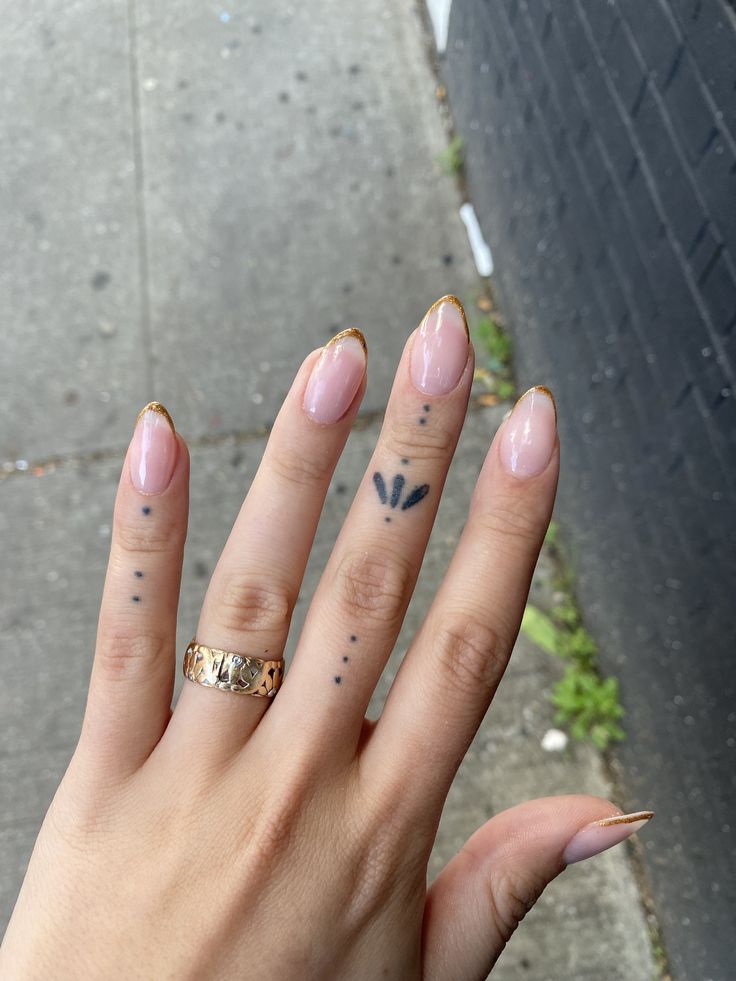 Chic Nude Nail Design with Golden Tips and Unique Tattoos for a Sophisticated Look.