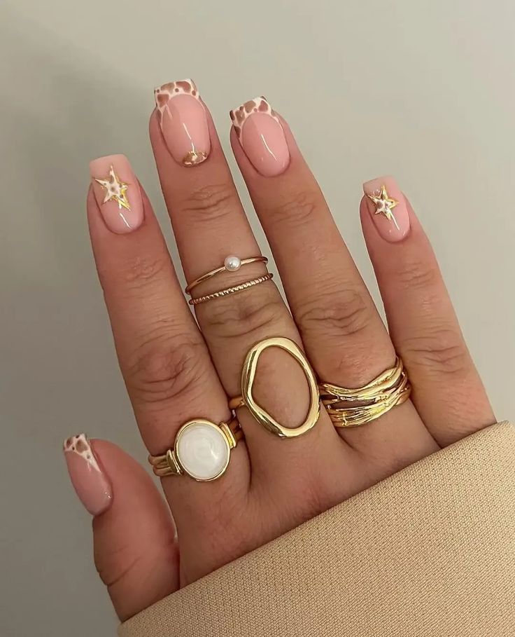 Sophisticated Soft Pink Nail Design with Trendy Animal Print and Playful Star Motifs, Accentuated by Elegant Gold Rings.