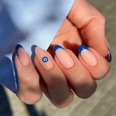 Elegant Nail Design: Soft Nude Base with Striking Blue Tips and Captivating Evil Eye Accents.