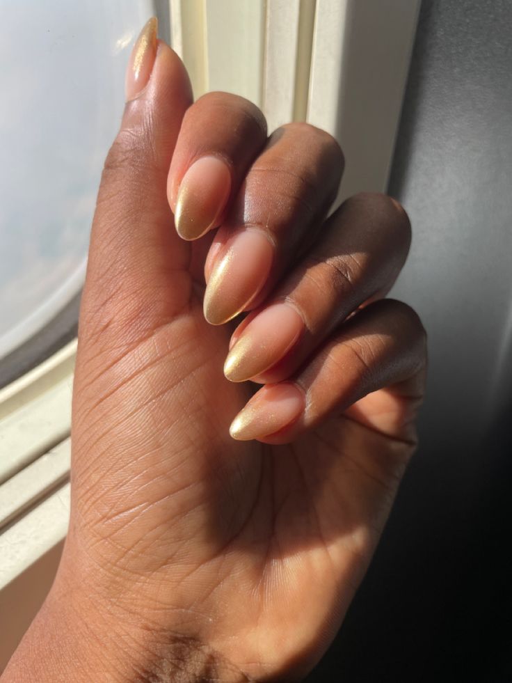 Elegant Almond-Shaped Nails with Gradient Nude and Shimmering Gold Tips for a Chic Look.