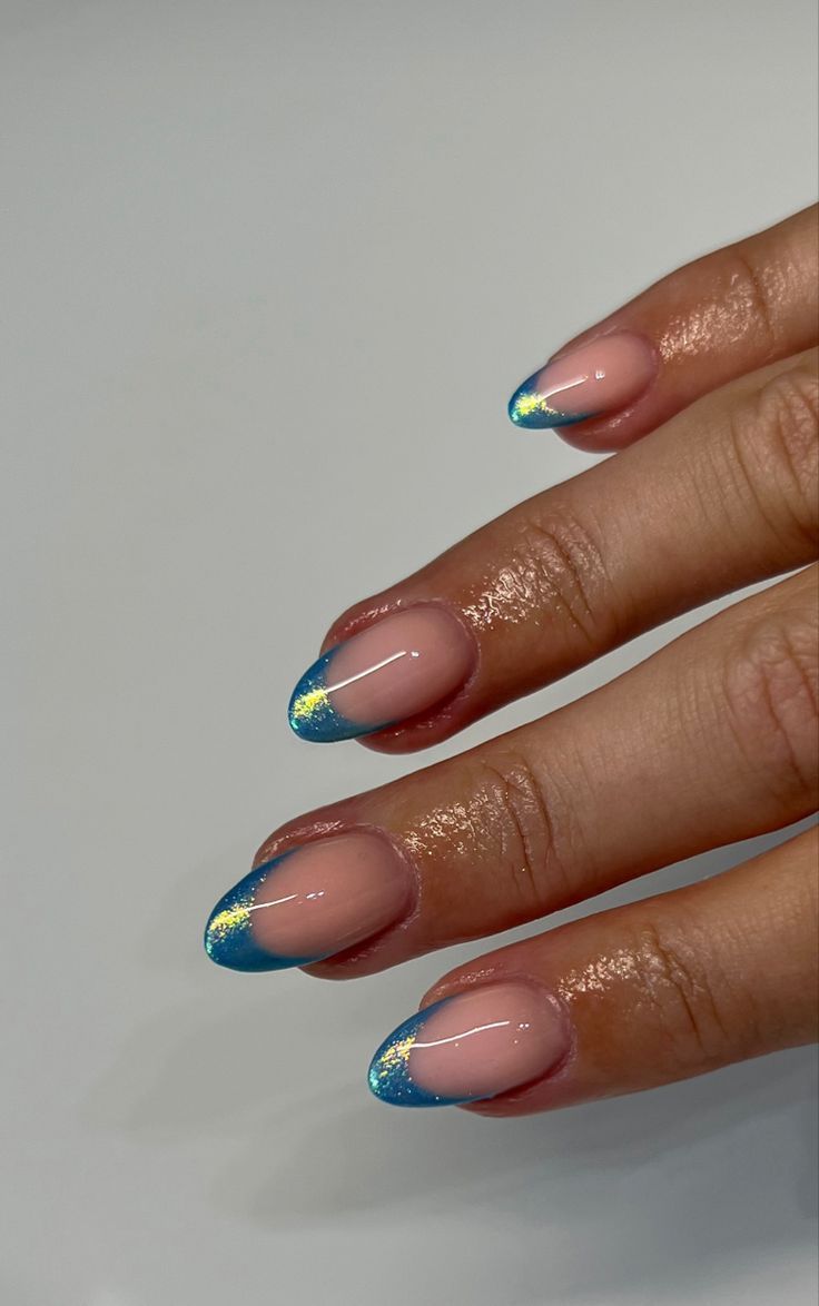 Chic Almond-Shaped Nail Design: Elegant Nude Base with Vibrant Blue Tips and Glitter Accents.