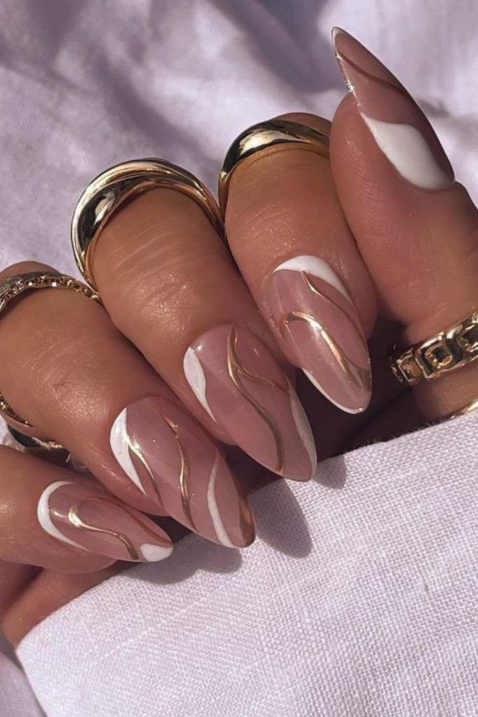 Sophisticated Almond-Shaped Nail Design in Soft Nude and White with Gold Accents and Glossy Finish.