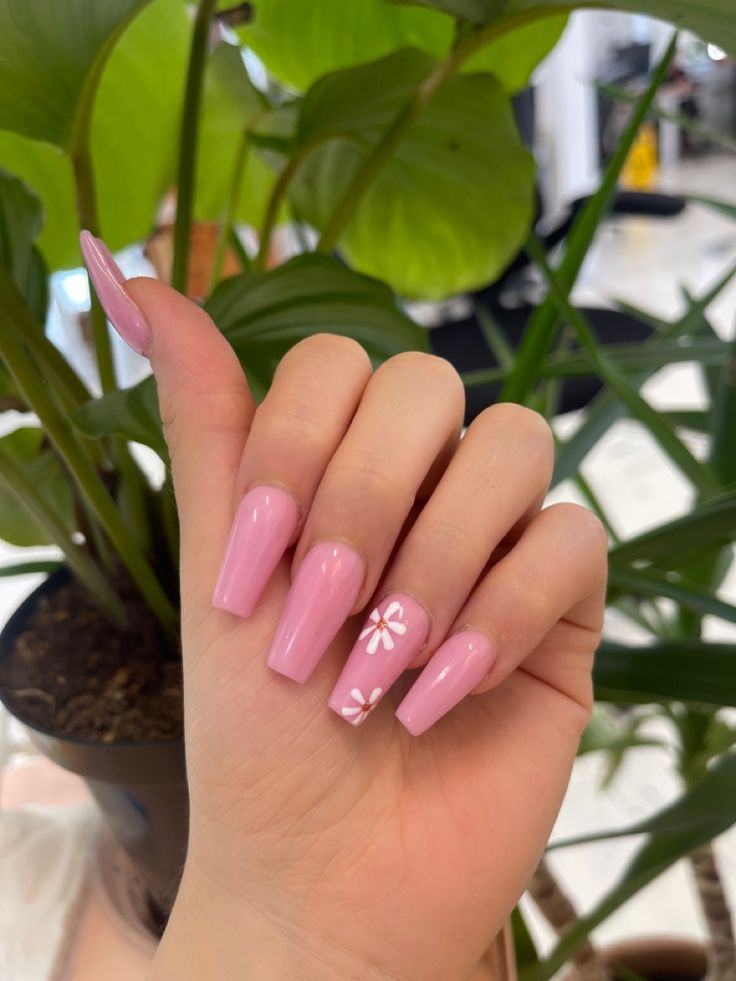 Charming Glossy Pink Nails with White Floral Accent Amidst Lush Greenery.