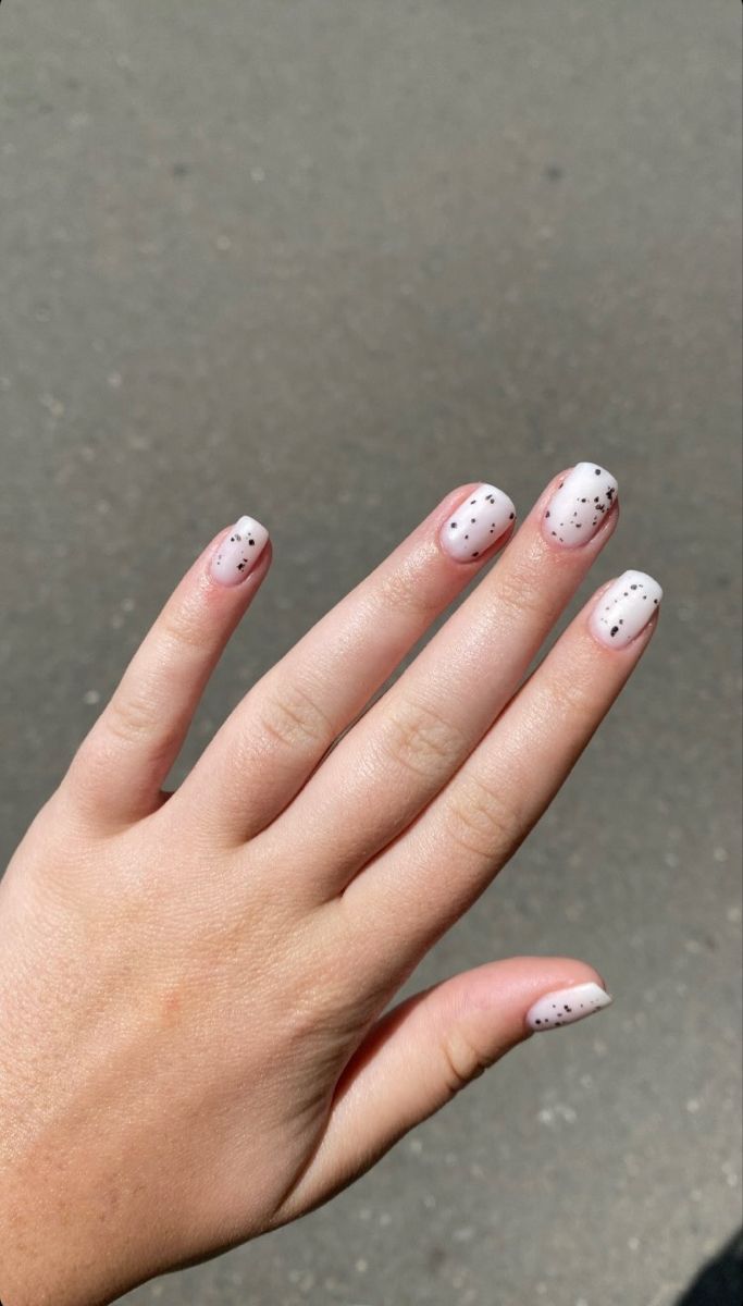 Chic Minimalist Nail Design: Soft White Base with Playful Black Speckles.