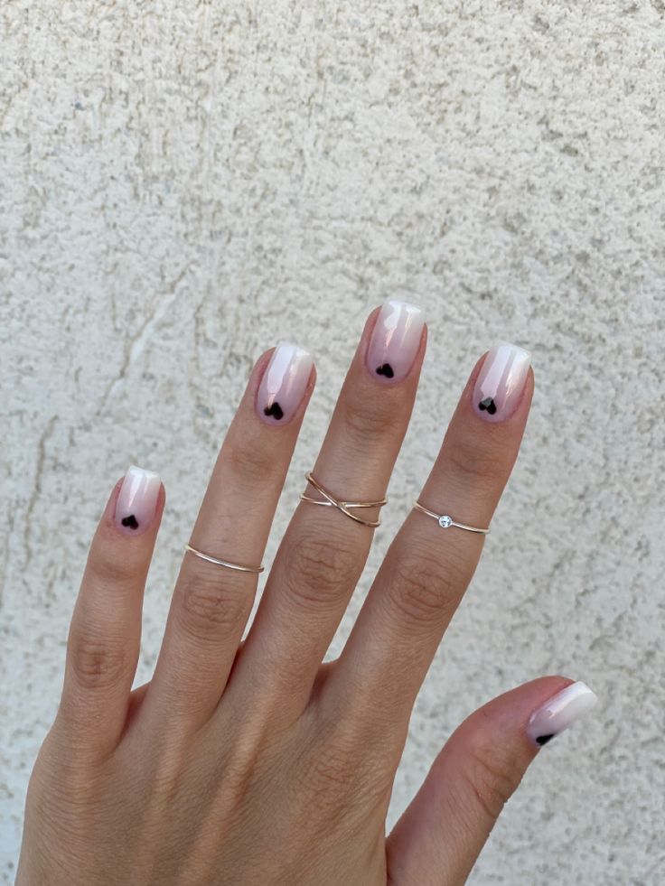 Elegant Chic Nail Design: Soft Pink Gradient with Black Heart Accents and Dainty Silver Rings