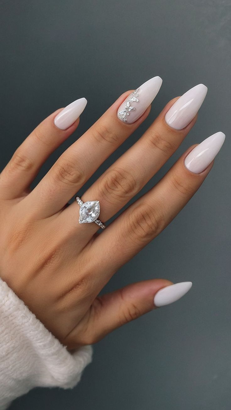 Chic Almond-Shaped White Nails with Glamorous Embellishments and Elegant Ring.