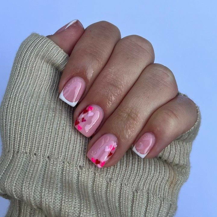 Romantic Whimsical Nail Design: Soft Pink Base with White French Tips and Vibrant Red Heart Motifs.