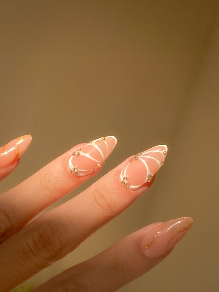 Sophisticated Nail Design: Soft Peach Base with Intricate White Patterns and Golden Accents