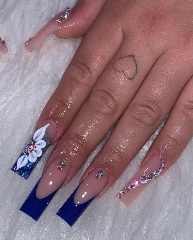 Sophisticated Nude and Vibrant Blue Nail Design with Floral Art and Glamorous Jewels