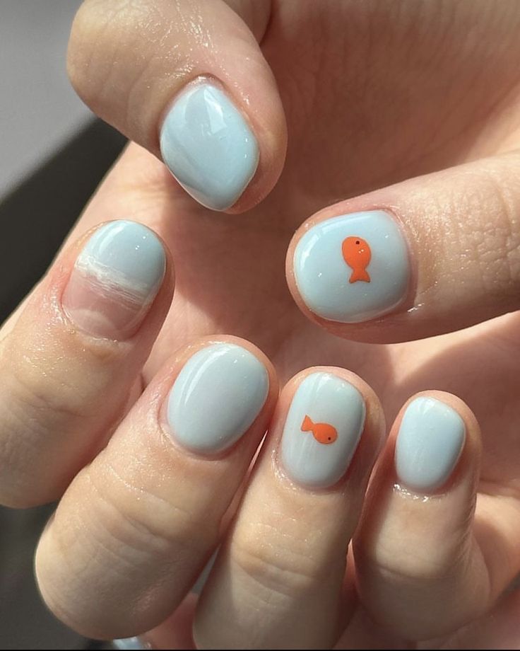 Whimsical Nail Design: Soft Blue Base with Playful Orange Fish Accents