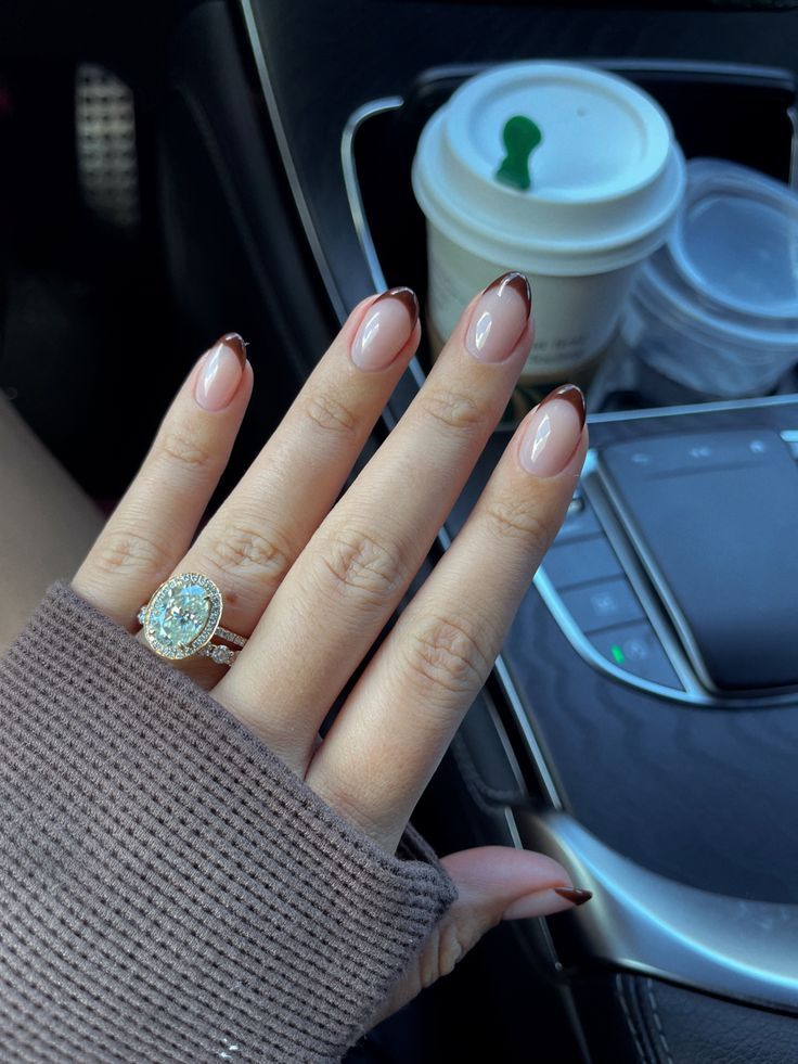 Sophisticated French Manicure: Chic Dark Brown Tips on Soft Nude Base Complemented by Sparkly Ring in Elegant Car Interior.