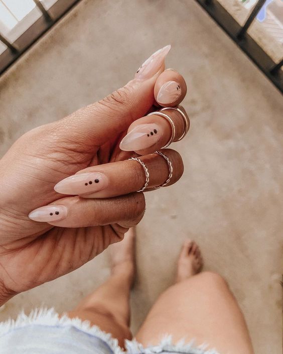 Chic Almond-Shaped Nail Design: Soft Nude Base with Subtle Black Dots and Minimalistic Rings.