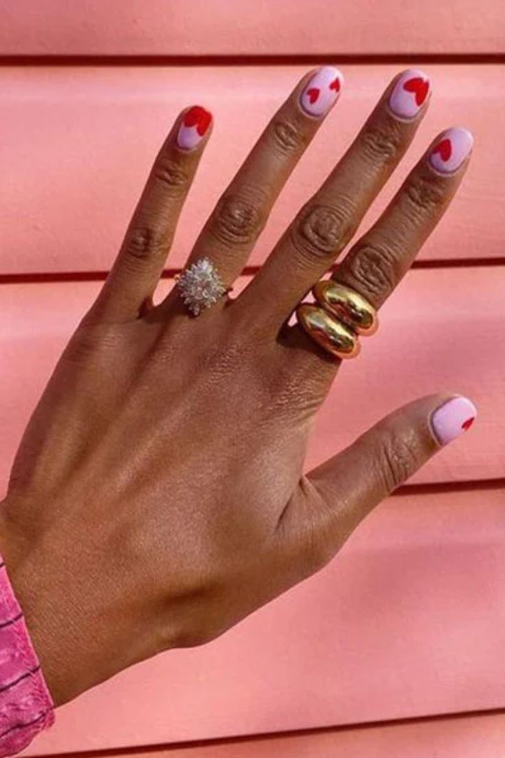 Playful Pink and Red Heart Nail Design with Elegant Ring Accessories.