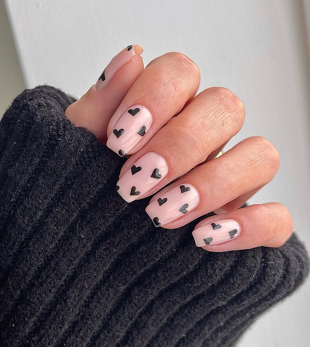 Whimsical Chic: Soft Nude Nails with Bold Black Heart Patterns