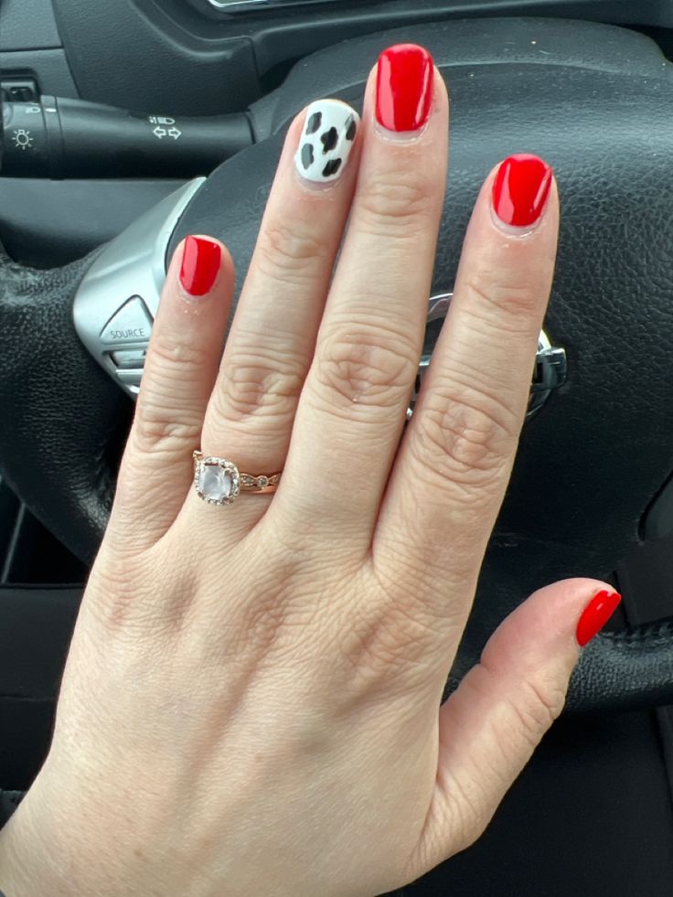 Striking Manicure: Vibrant Red Nails with Playful Spotted Accent and Elegant Ring.