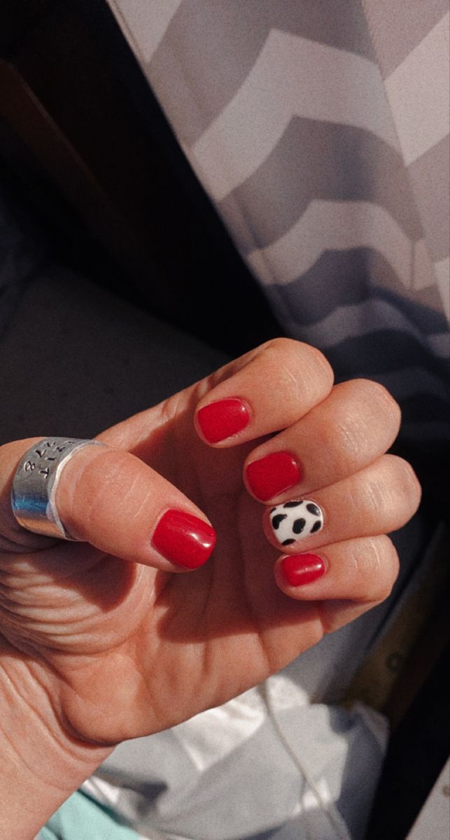 Vibrant Red Manicure with Playful Cow Print Accent Nail: A Blend of Elegance and Quirkiness.