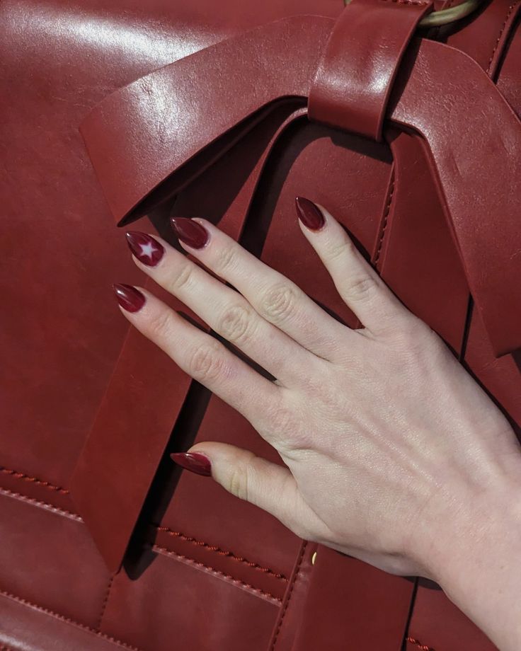 Chic Almond-Shaped Red Manicure with Bold Star Accent and Coordinating Handbag.