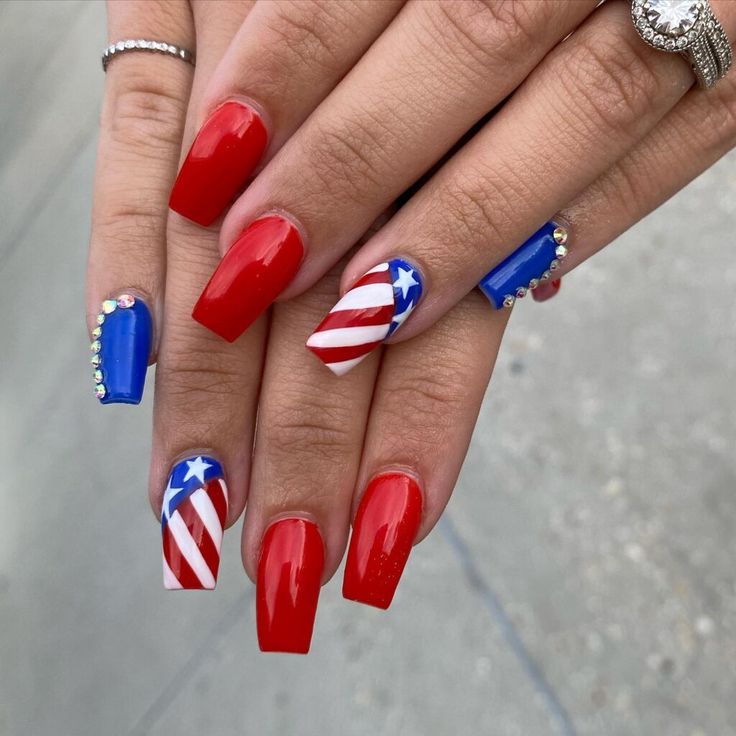 Festive Patriotic Nail Design: Bold Red with Striking Blue Accents and Glamorous Embellishments