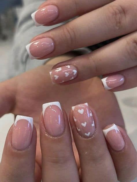 Romantic Manicure: Classic French Tips Meets Playful Heart Patterns in Nude Tones.