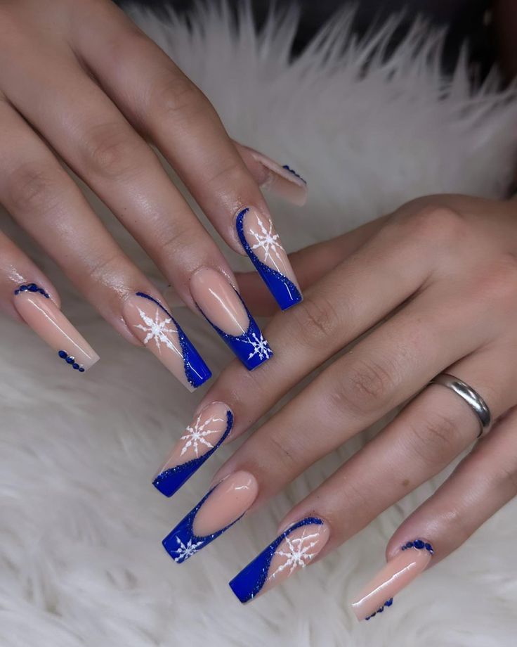 Chic Festive Long Nails: Stylish Nude and Deep Blue with Snowflake Designs and Shimmering Accents.