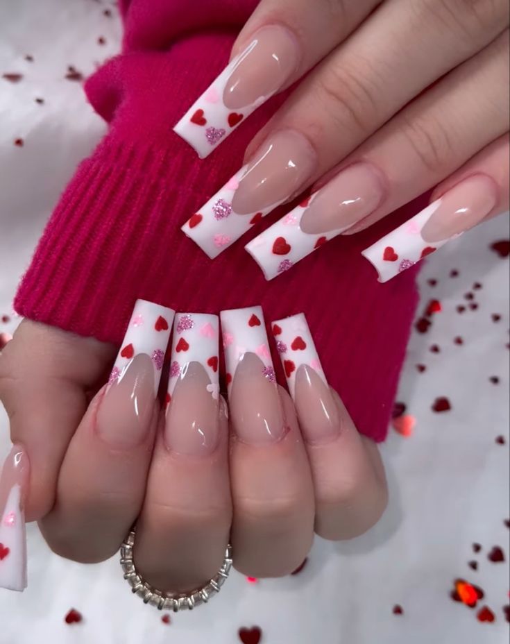 Whimsical Nail Design: Long Square Tips with Sheer Nude Base, Vibrant White Tips, and Playful Red Hearts for Festive Charm.