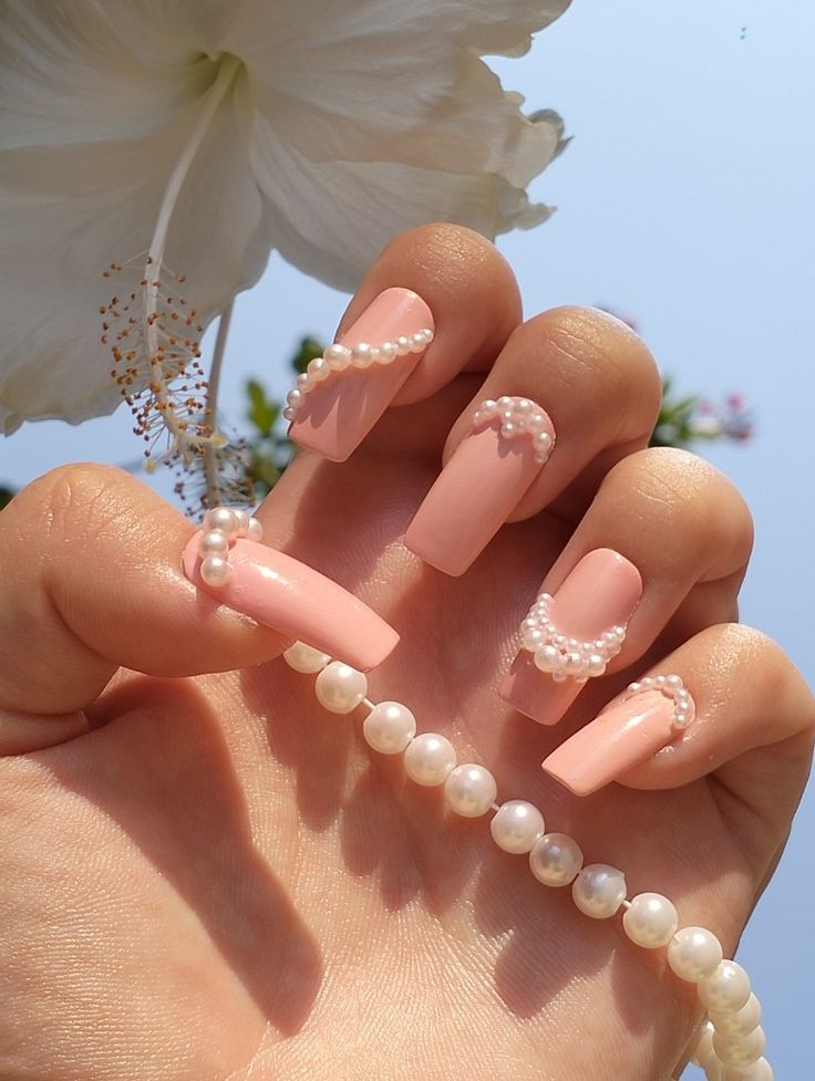 Sophisticated Elongated Peach Nail Design with Delicate Pearl Accents and Floral Background.