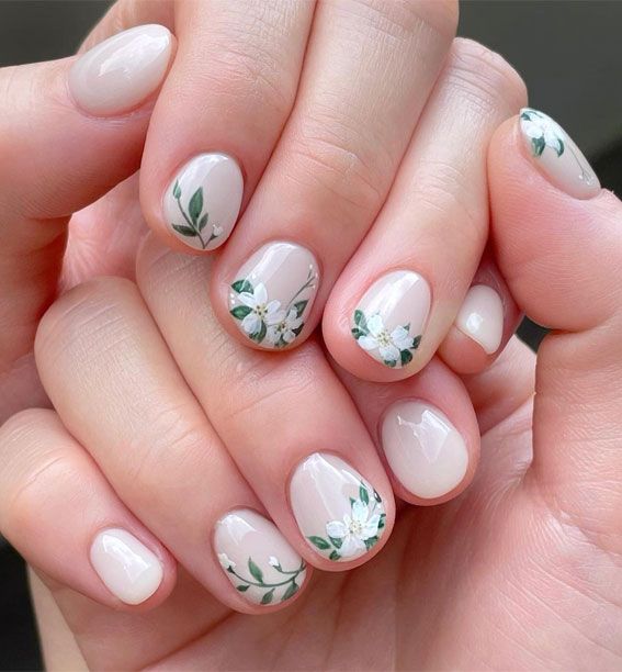 Elegant Floral Nail Design: Soft Nude Base with Intricate White Blossoms and Leafy Green Accents.