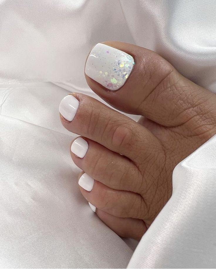 Pristine White Pedicure with Iridescent Glitter Accent for a Fresh Summer Look.