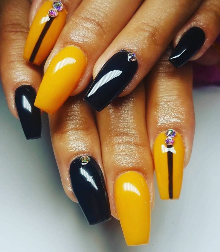 Chic Black and Yellow Nail Design with Glossy Finish, Rhinestone Accents, and Playful Stripes.