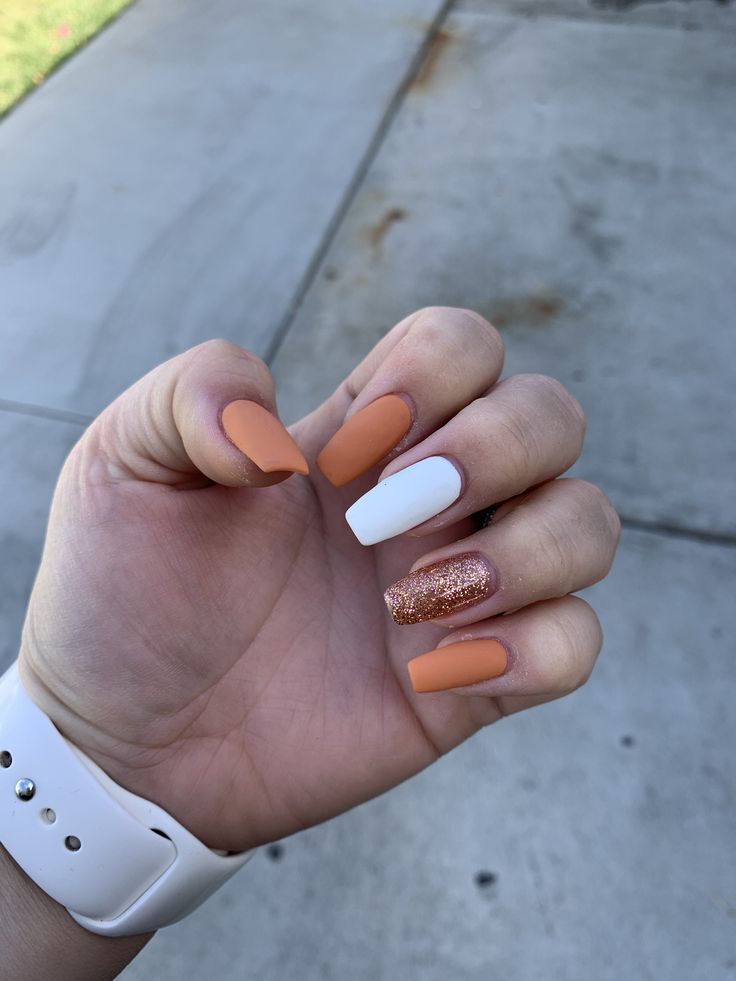 Vibrant Nail Design: Matte Orange, Glossy White, and Glittery Gold Accents.