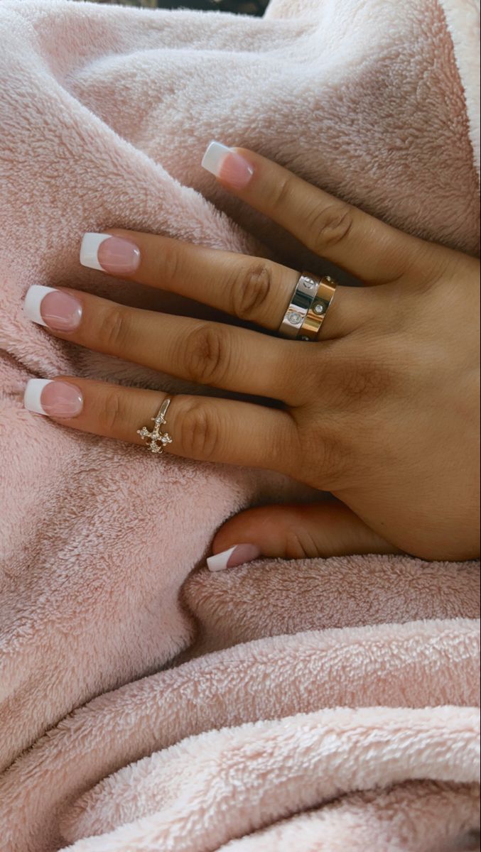 Chic French Manicure with Pink Base and White Tips, Accentuated by Glamorous Rings and Cozy Aesthetic