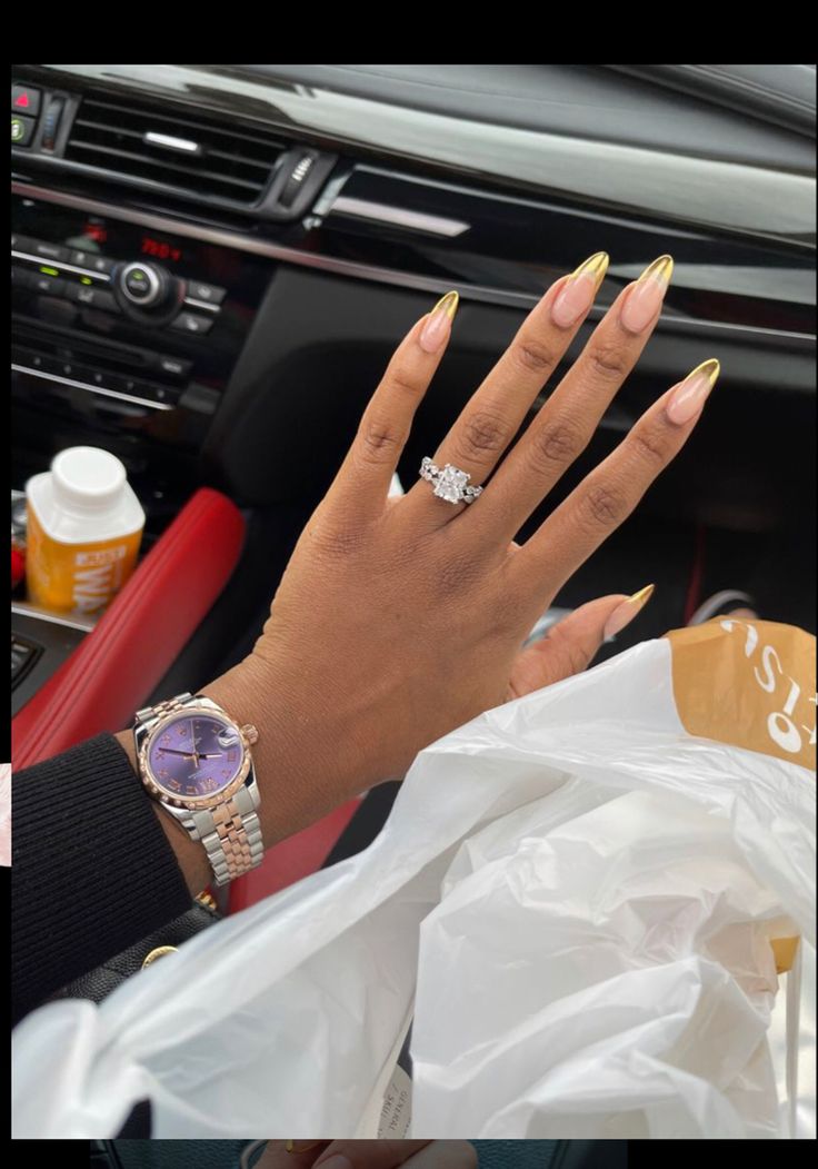 Chic Almond-Shaped Gold Nail Design Complemented by Stylish Accessories in a Luxurious Red-Car Interior.