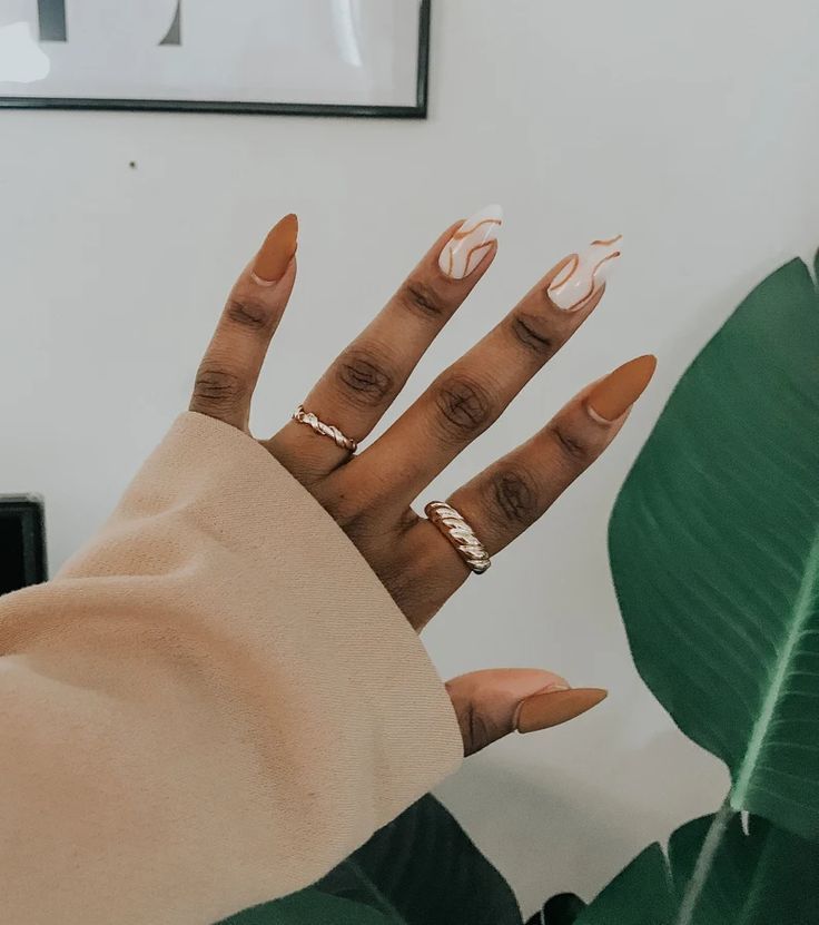 Chic Almond Nail Design with Nude Base, White Swirls, and Metallic Accents