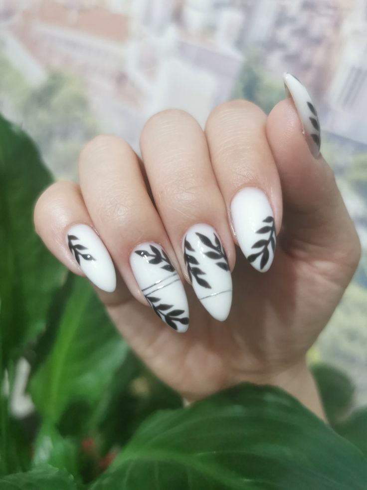 Elegant Matte White Nail Design with Glossy Accents and Black Leaf Patterns.