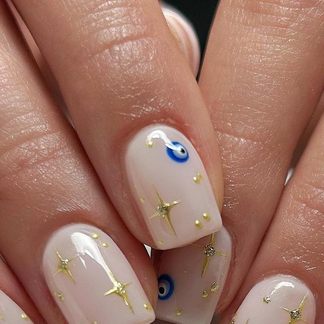 Chic Nude Nail Design with Shimmering Gold Accents and Stunning Blue Eye Motif