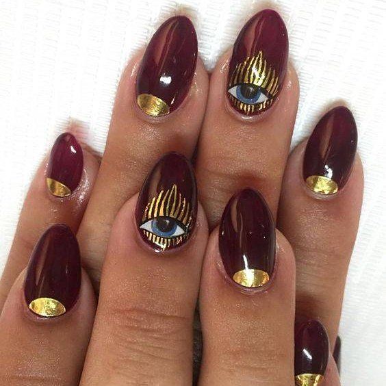 Elegant Burgundy Nail Design with Intricate Gold Accents and Mystical Eye Motifs.