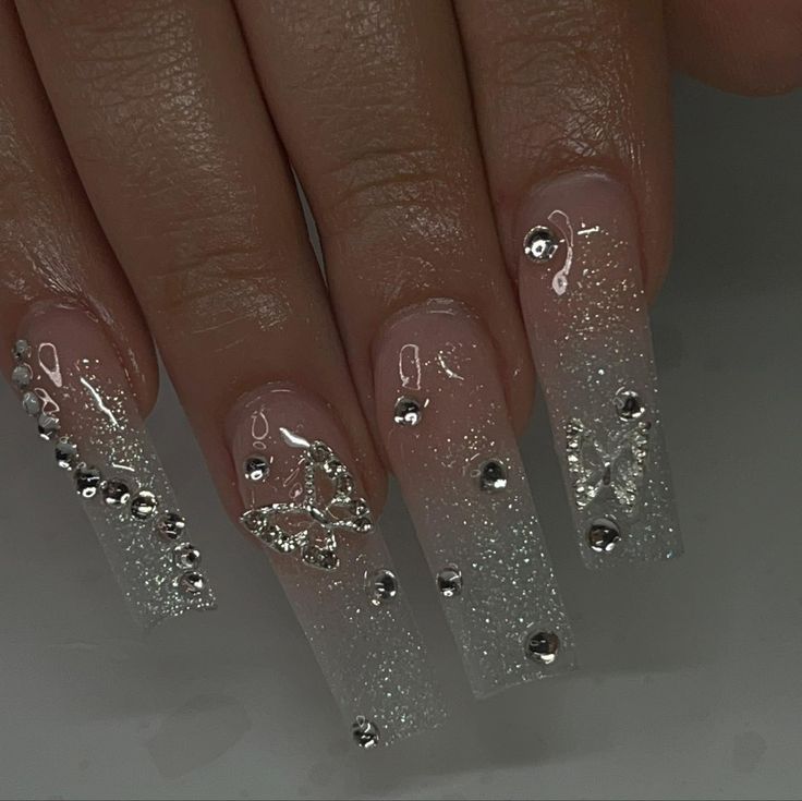 Elegant Glittering Ombre Nails with Delicate Silver Embellishments and Sparkling Butterfly Designs.