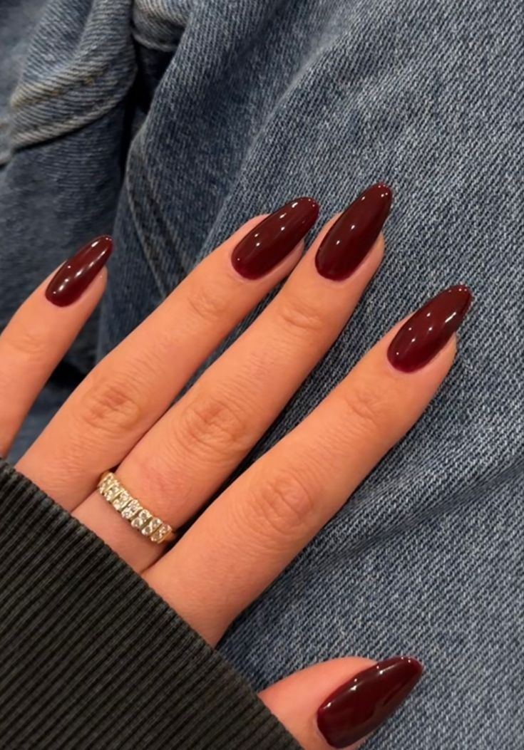 Sophisticated Almond-Shaped Burgundy Nails with Glossy Finish and Diamond Ring Enhance Casual Denim Look.