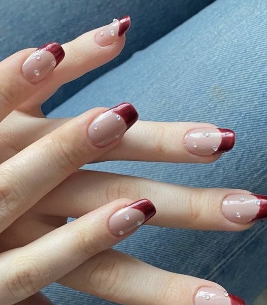 Chic Nude and Deep Red French Tip Nail Design with Rhinestone Accents.