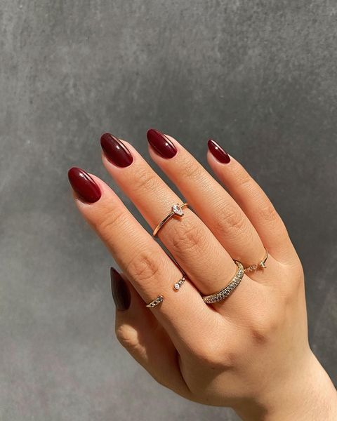 Chic Burgundy Almond Nails Enhanced by Delicate Gold Rings for Glamorous Occasions.